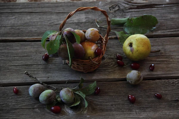 Nature morte avec des prunes fraîches dans un panier en osier et des poires — Photo