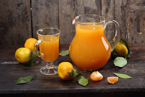 Tangerine juice in the clear jug on a wooden table — Stock Photo, Image