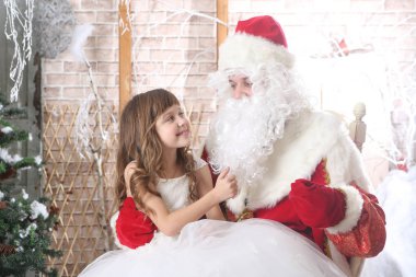 Noel Baba'ya dizlerinin üzerinde bir bebek tutan kırmızı bere