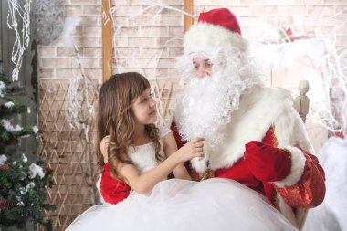 Noel Baba'ya dizlerinin üzerinde bir bebek tutan kırmızı bere