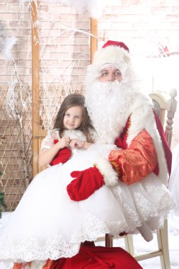 Noel Baba'ya dizlerinin üzerinde bir bebek tutan kırmızı bere