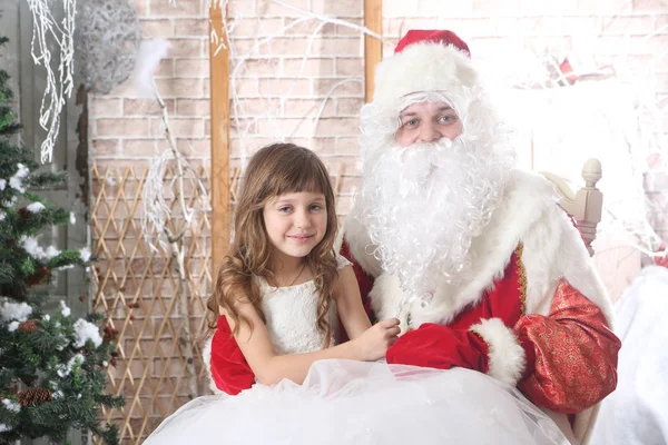 Noel Baba'ya dizlerinin üzerinde bir bebek tutan kırmızı bere