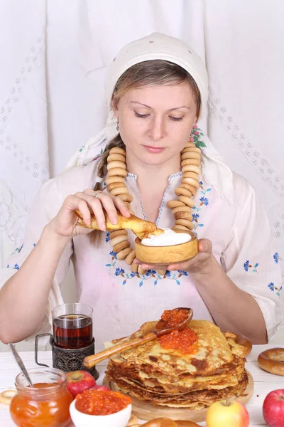 Menina em um cachecol comendo panquecas com creme azedo — Fotografia de Stock