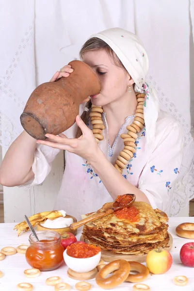 Het meisje aan de feestelijke tafel pannenkoeken eten en het drinken van melk — Stockfoto