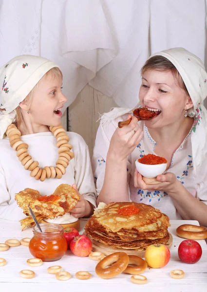 Мама з дочкою їсть млинці з червоною ікрою на святі та — стокове фото