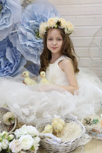 Menina em uma grinalda e um vestido branco brincando com um pato vivo — Fotografia de Stock