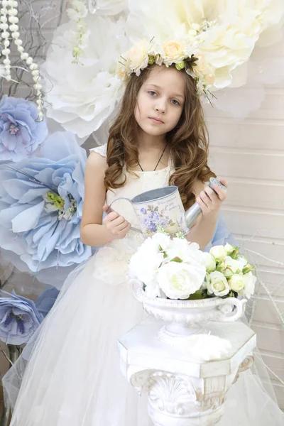 Niña en una corona y un vestido blanco regando flores —  Fotos de Stock