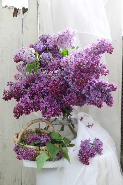 Lilás. ramo de lilás em um frasco de vidro e cesta de vime — Fotografia de Stock