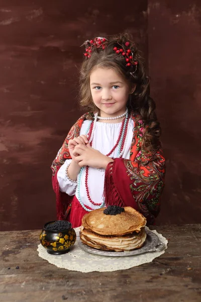 在俄罗斯服装的女孩和煎饼黑鱼子酱在木桌上 — 图库照片
