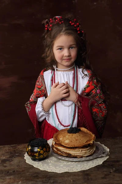 在俄罗斯服装的女孩和煎饼黑鱼子酱在木桌上 — 图库照片