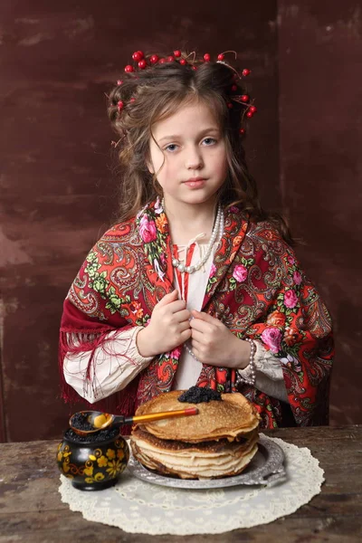A girl in Russian dress keeps pancakes with black caviar. A girl in a Russian dress keeps pancakes with black caviar