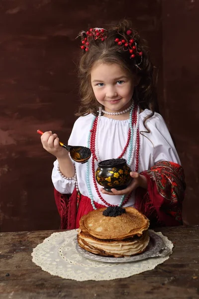 ロシアの衣装で女の子はブラック キャビアとパンケーキを食べる ロシアのドレスの少女を保つブラック キャビアとパンケーキ — ストック写真