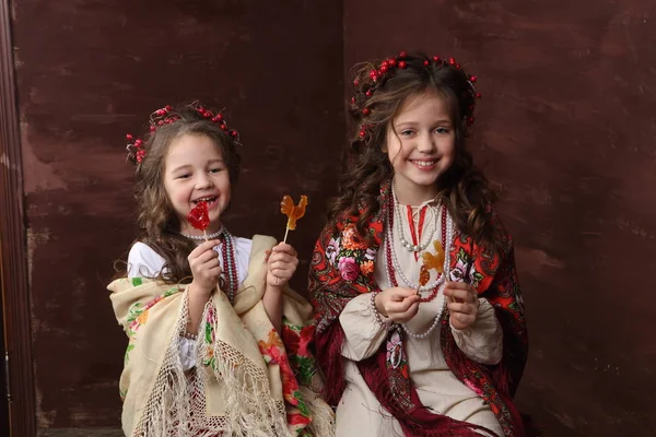 Girls in Russian dresses laugh and hold lollipops