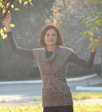 Sonbahar parkında sarı yapraklı bir ağacın yanındaki kız.