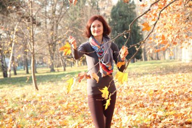 Sonbahar parkında sarı ve kırmızı yapraklı ağacın yanındaki kız.