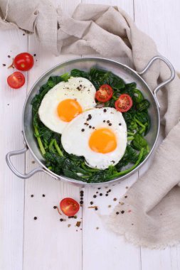 Beyaz ahşap arka planda ıspanaklı ve domatesli sahanda yumurta.