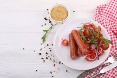 Kızarmış sosis, domates, soğan, roka ve hardal, beyaz ahşap arka planda.