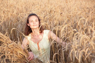 Köylü kızı tarlada buğday kulaklarına sarılıyor.