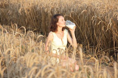 Köylü kızı buğday tarlasında süt içiyor.