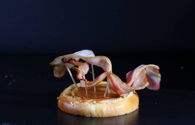 Hamburger ekmeğinde ızgara pastırma. Siyah arkaplanda ekonomi