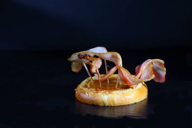 Hamburger ekmeğinde ızgara pastırma. Siyah arkaplanda ekonomi