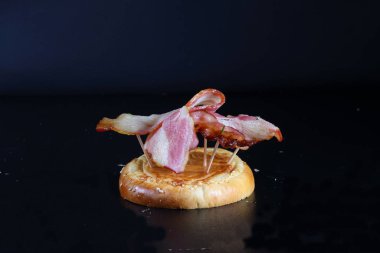 Hamburger ekmeğinde ızgara pastırma. Siyah arkaplanda ekonomi