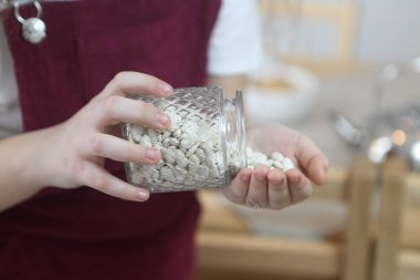 Kız kavanozdan avuç içine fasulye döküyor.