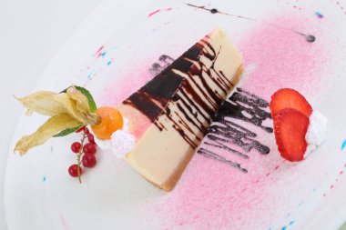 Çilekli cheesecake, frenk üzümü ve bitki salatası beyaz arka planda.