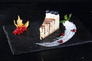 Siyah arka planda yaban mersinli, üzümlü ve çikolatalı cheesecake.