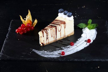 Siyah arka planda yaban mersinli, naneli ve çikolata soslu cheesecake.