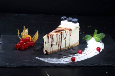 Siyah arka planda yaban mersinli, üzümlü ve çikolatalı cheesecake.
