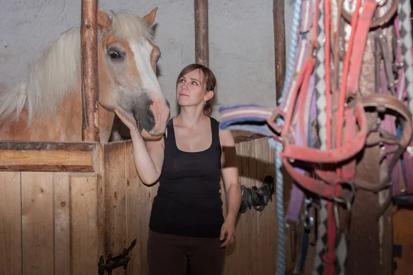 Jonge vrouw streelde haar paard in stal. — Stockfoto