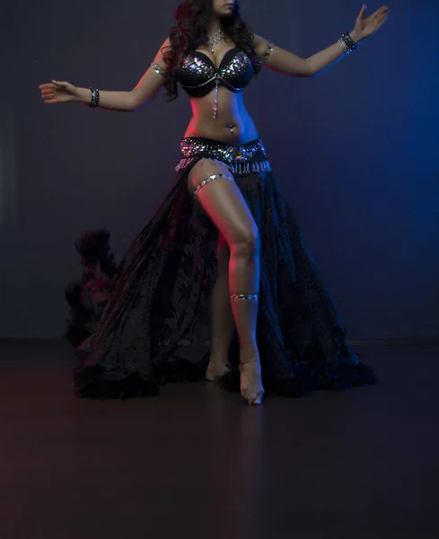 Sexy schlanke Frau, Bauchtänzerin im schwarzen Kostüm mit Kristallen. dunkler Hintergrund mit rosa und blauen Blitzen — Stockfoto