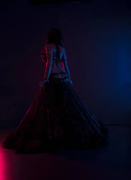 Mulher magra sexy, dançarina de barriga em traje preto com cristais. Fundo escuro com luz rosa e azul, de volta — Fotografia de Stock