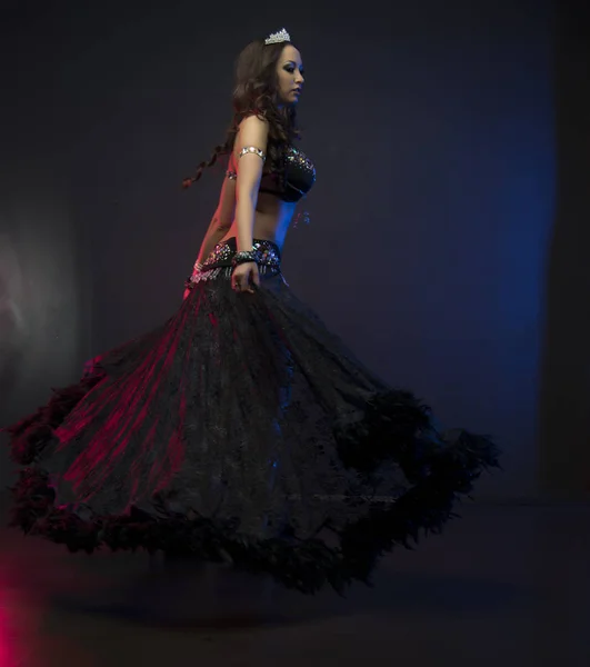 Mujer delgada sexy, bailarina del vientre en traje negro con cristales. Fondo oscuro con aligeramiento rosa y azul — Foto de Stock