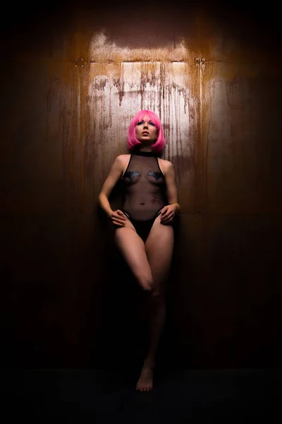 Sexy woman pink wig in black transparent bodysuit with bats on nipples posing against metal wall — ストック写真