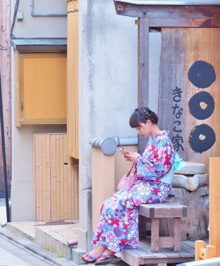 Genç kadın giymek ahşap bankta oturan ve cep telefonu çalmaya Kimono