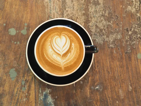 A cup of coffee with heart pattern in a black cup. — Stock Photo, Image