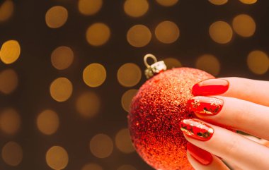 Kırmızı manikürlü kadın eli Noel balosunu tutuyor.