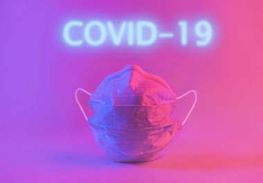 Tıbbi koruyucu maske ve neon pembe ışıkla yazılmış COVID 19. Yaratıcı modern kavram.