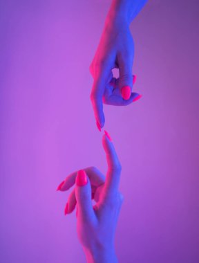 Parlak manikürlü iki kadın el, Adem 'in neon ışıktaki işareti gibi birbirlerine uzanıyorlar. Canlı renk.