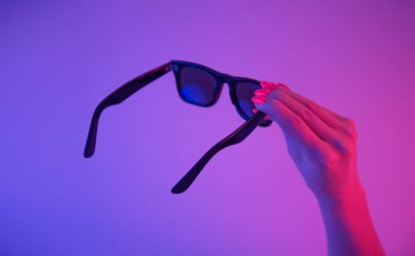 Parlak turuncu manikürlü, neon ışıklı bir kadın elinde siyah güneş gözlüğü..