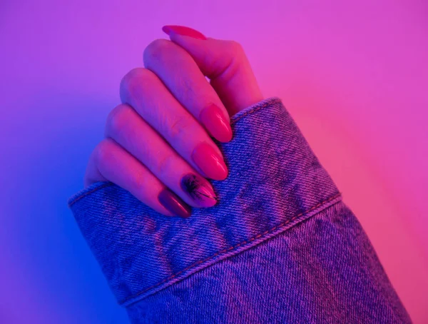 Woman hand with retro wave color and palm tree design on nails in neon pink and blue light. Trendy synthwave manicure. Vibrant color.