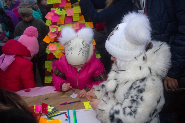 Донецк, Украина - 23 декабря 2016 года: Дети пишут на этикетках на символическом дереве на площади Ленина с пожеланиями мира — стоковое фото