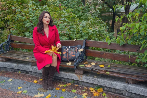Задумчивая женщина в красном пальто на скамейке в осеннем парке. Люди — стоковое фото
