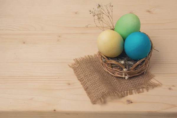 Пасхальные яйца в плетеной корзине на деревянной поверхности — стоковое фото