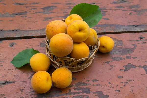 Albaricoques maduros en una canasta de mimbre sobre una superficie de madera — Foto de Stock