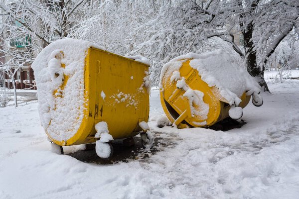 Yellow trash can covered with snow. Municipal economy
