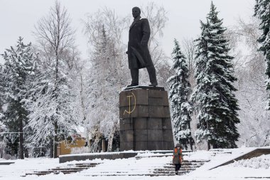 Makeevka, Ukrayna - 22 Kasım 2017: Kar komünist lider Lenin karla kaplı bir şehirde Anıtı yakınındaki bir turuncu yelek kadında temizler