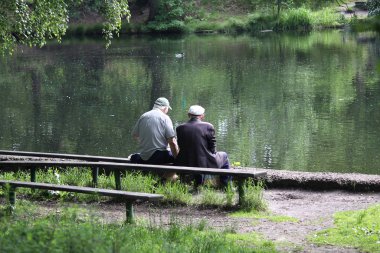 Göletin yanındaki bankta oturan iki yaşlı adam. İnsanlar
